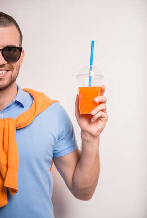 Portrait of cheerful young man drinking juice on a gray backgroundの写真素材