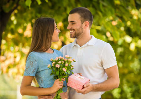 Loving young couple on a date with flowers and with a gift in the parkの写真素材