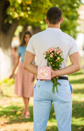 Loving young couple on a date with flowers and with a gift in the parkの写真素材