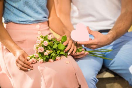 Loving young couple on a date with flowers and with a gift in the parkの写真素材