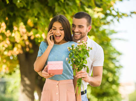 Loving young couple on a date with flowers and with a gift in the parkの写真素材
