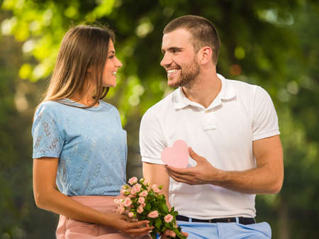 Loving young couple on a date with flowers and with a gift in the parkの写真素材