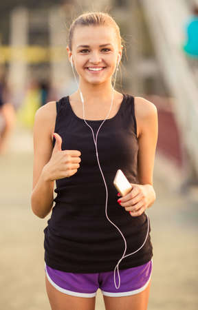 The young beautiful girl with headphones running and doing fitness in cityの写真素材