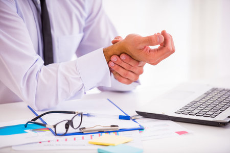 Illness hand. Portrait of a businessman with a beard while working in his office, holding hand