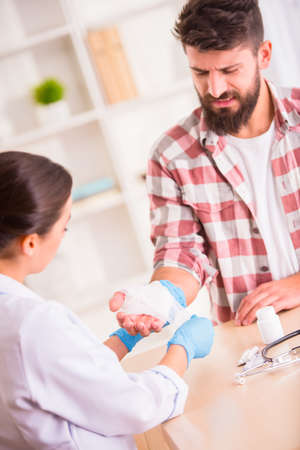 Injury hands. Young man with injured hands. Young woman doctor helps the patientの写真素材