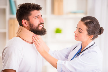 Injury neck. Young man with injured neck. Young woman doctor helps the patientの写真素材