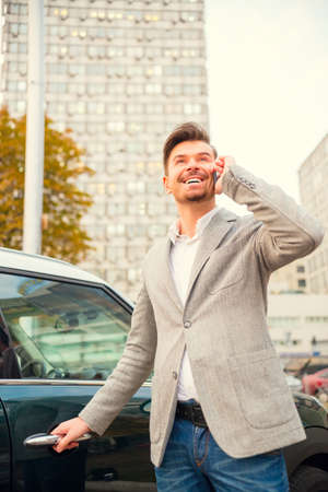 Portrait of a young successful businessman in front of his car on a background of office centerの写真素材