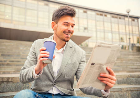 Portrait of a young successful businessman sitting on stairs and reading a newspaper on a background Business Centreの写真素材