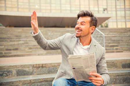 Portrait of a young successful businessman sitting on stairs and reading a newspaper on a background Business Centreの写真素材