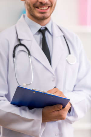Young doctor with a stethoscope in a white robe holding a card. Close-upの写真素材