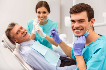 Young dentist and his assistant treating elderly manの写真素材