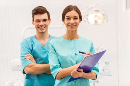 Portrait of happy young doctor and female assistant with clipboard in dental clinicの写真素材