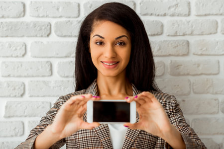 Beautiful African American girl hold the phone in hands on a gray background