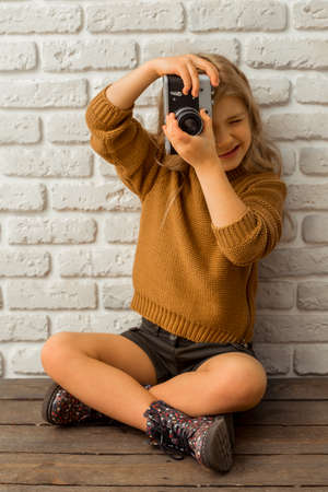 Pretty little blonde girl making a photo while sitting cross-legged against white brick wallの写真素材