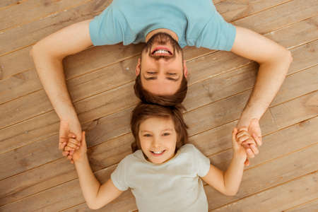Top view of handsome young father and his cute little son lying head to head on a wooden floor and holding handsの写真素材