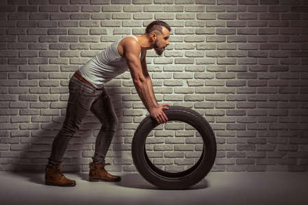 Side view of stylish man with beard leaning on a tire, standing against brick wallの写真素材