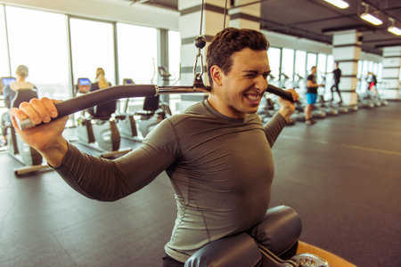Attractive young muscular man working out on a fitness station in gym, pumping iron