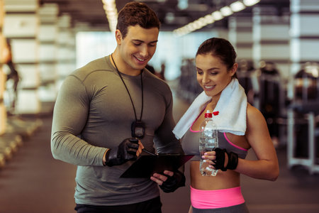 Handsome muscled male trainer consulting attractive young female in gym, both smilingの写真素材