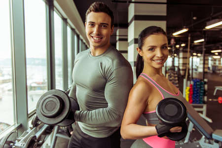 Attractive young muscular people working out with dumbbells in gym, looking at camera and smilingの写真素材