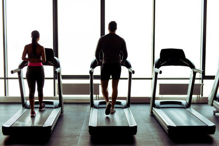 Back view of attractive young muscular man and woman running on a treadmill in gym