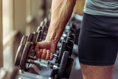 Handsome young muscled man working out with dumbbells in gym, close-upの写真素材