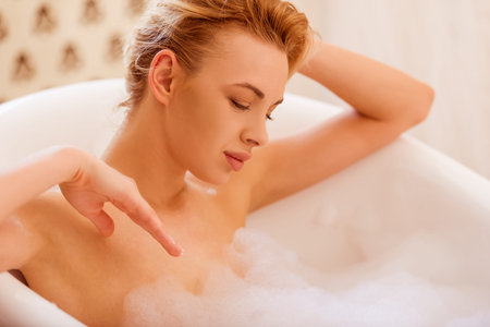 Beautiful young blonde woman enjoying pleasant bath with foam, close-up