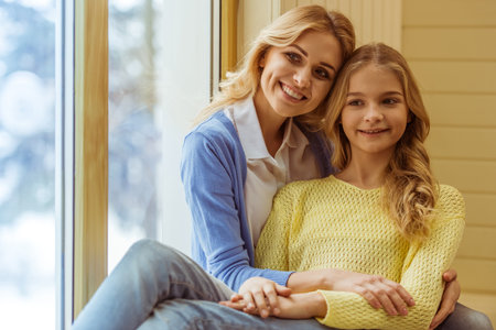 Lovely teenage girl and her beautiful mother cuddling, looking at camera and smilingの写真素材