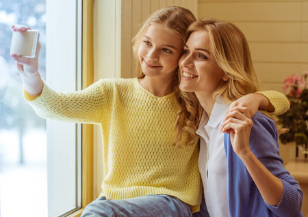 Lovely teenage girl and her beautiful mother cuddling, making a photo and smilingの写真素材