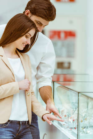 Happy beautiful young couple choosing a wedding rings and smiling while doing shopping in mallの写真素材