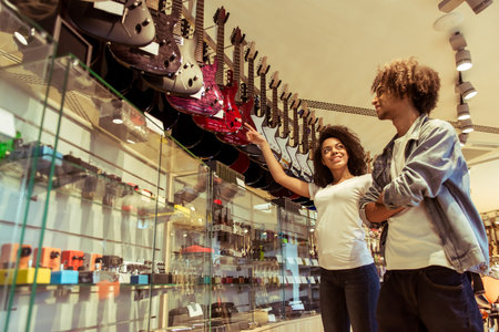 Beautiful young Afro-American couple smiling while choosing an electric guitar in a musical shop
