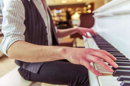 Handsome stylish man in classical vest playing a piano in a musical shop, close-upの写真素材