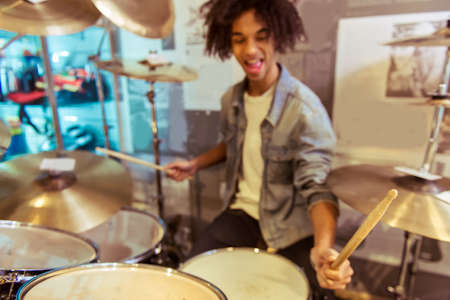 Handsome young Afro-American man in jeans jacket smiling while playing drums in a musical shopの写真素材