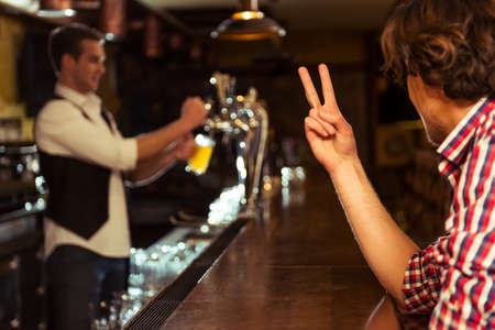 Side view of man in casual clothes ordering beer while sitting at bar counter in pub, a bartender in the backgroundの写真素材