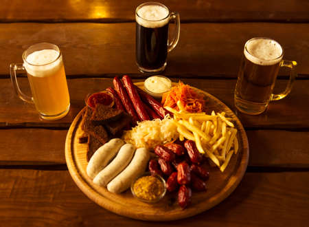Top view of big wooden tray with delicious snacks and glasses of beer, on wooden backgroundの写真素材
