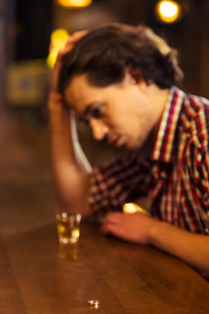 Sad man in casual clothes is leaning on bar counter in pub, a glass of alcoholic beverage near, in...