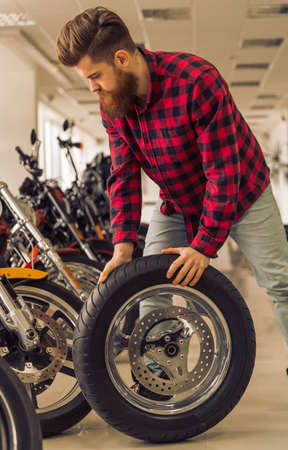 Handsome young bearded man in casual clothes is repairing a motorbikeの写真素材