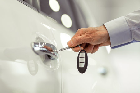 Middle aged businessman in classic shirt is opening a car with a key in a motor show, close-up