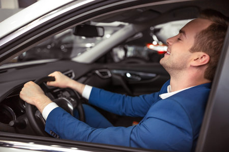 Side view of handsome young businessman smiling while sitting in car in a motor show