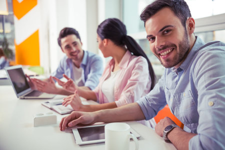 Young freelancers are using gadgets, talking and smiling while working at the modern office