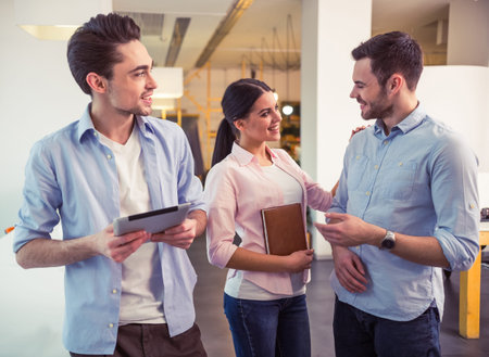 Young freelancers are using gadgets, talking and smiling while standing at the modern officeの写真素材