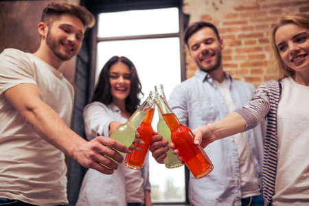 Young people in casual clothes are resting, clanging bottles of drink together and smilingの写真素材