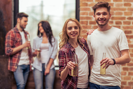 Two beautiful young couples in casual clothes are resting with bottles of drink, talking and smilingの写真素材