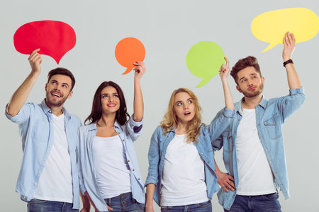 Beautiful young people in jeans are holding colorful speech bubbles and showing emotions, standing on a gray backgroundの写真素材