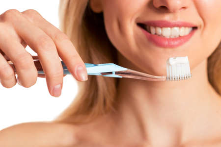 Beautiful young woman holding a toothbrush with toothpaste and smiling, isolated on a white background, croppedの写真素材
