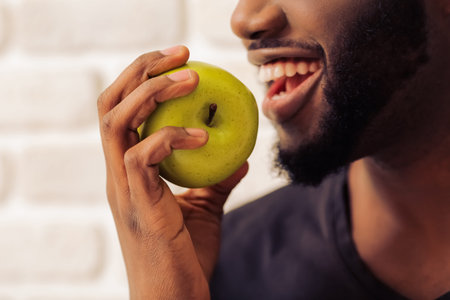Side view of handsome Afro American man in casual clothes holding an apple and smiling, against...
