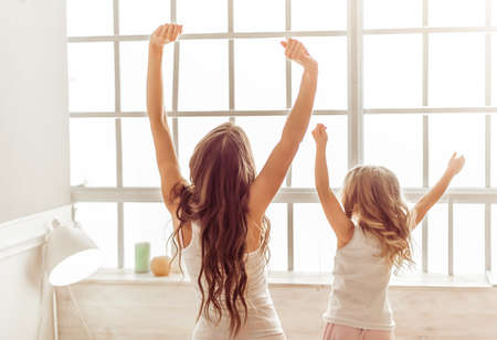 Back view of beautiful young mother and her cute little daughter stretching and yawning in the morningの写真素材