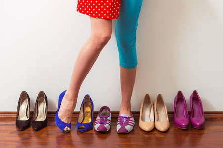 Beautiful girl with one leg in sports shoe and another in high heeled shoe is standing in a row with dress shoes, croppedの写真素材