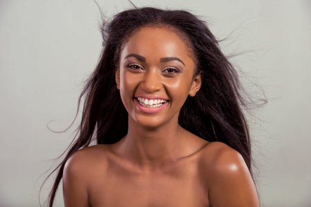Portrait of happy beautiful Afro American girl with flying hair looking at camera and smiling, on a...