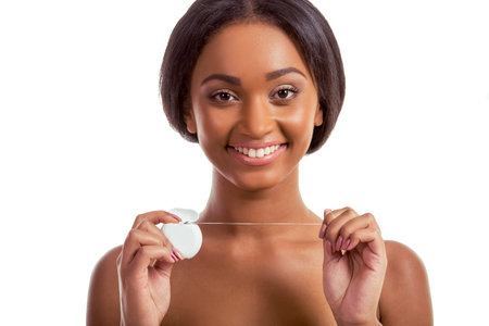 Portrait of beautiful Afro American girl holding a dental floss, looking at camera and smiling, on a...