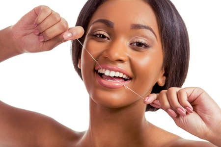 Portrait of beautiful Afro American girl using a dental floss, looking at camera and smiling, on a white background, close upの写真素材